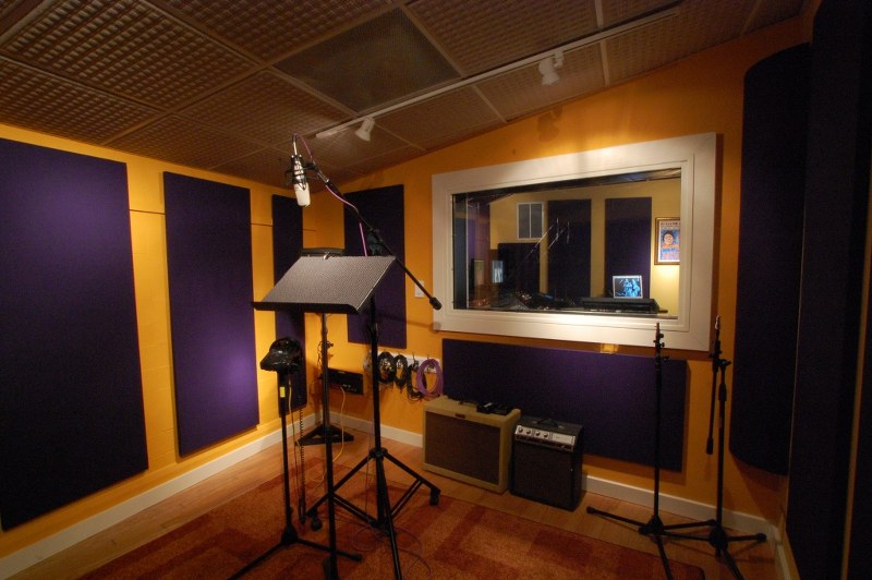 Photo of the recording booth in the Bob Dylan suite at the Washington DC studios of Clean cuts. A professional microphone stands in the center of the room surrounded by colorful acoustical wall panels.